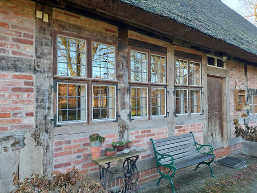 Uenzen, Hofstelle, Nordseite mit saniertem Fachwerk, Klöntür und an den Ständern angeschlagenen Fenstern und dem 2005 eingedecktem Reetdach (2023) Ursprünglich befanden sich lediglich das mittlere und das rechte Fenster sowie eine Tür in der Lucht. © Interessengemeinschaft Bauernhaus, Jenny Heinrichsdorff-Struß und Herbert Struß
